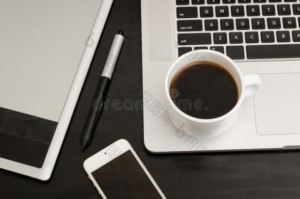 咖啡杯，带有手写笔的图形平板电脑，黑色木制桌子上的笔记本电脑和手机的一部分，特写