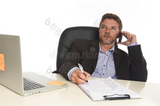 穿西装的商人在笔记本电脑办公桌上工作，在现代办公室用手机说话