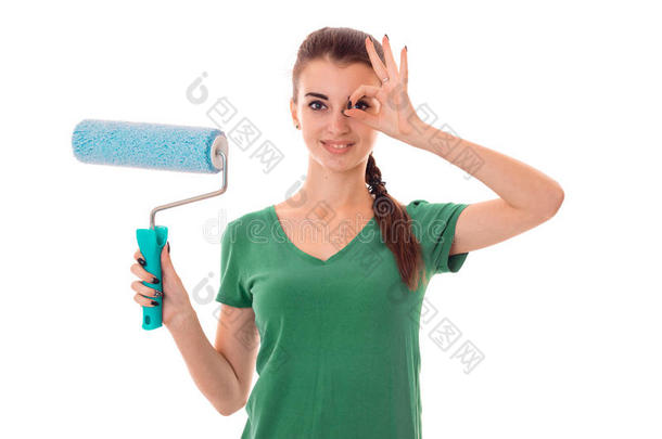一个年轻的女孩穿着一件绿色的t恤，拿着一个滚筒来画白色背景上孤立的墙壁