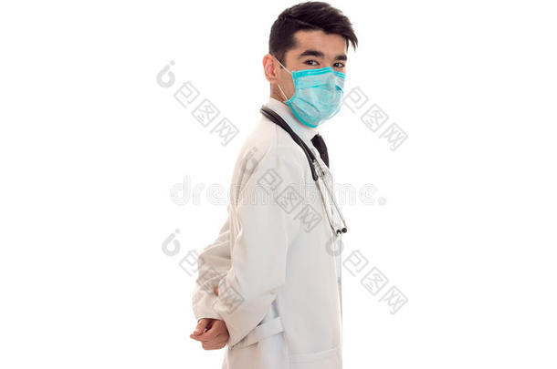 穿着白色实验室外套的医生侧身站着，脸上戴着白色背景上隔离的面具