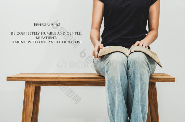 随便的年轻女人拿着一本公开的圣经以弗所书4：2在她的腿上。