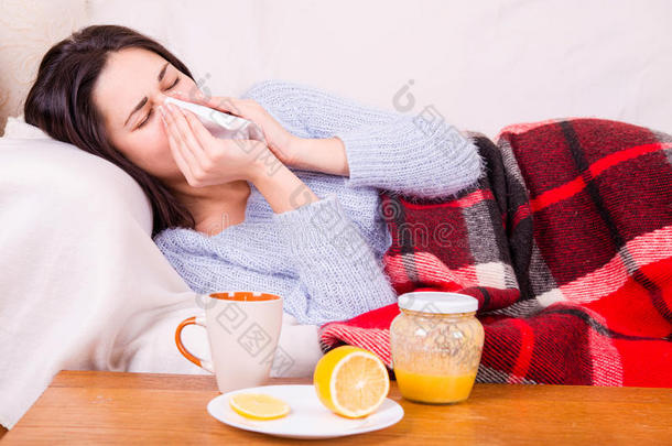 感冒的女孩躺在毯子下拿着纸巾