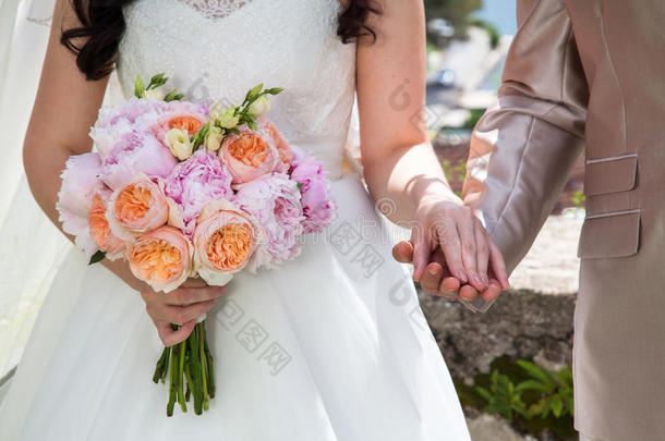 婚礼上的新娘和新郎用橙色玫瑰和粉红色牡丹的婚礼花束牵手。