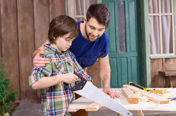 父亲看着集中的儿子锯木板