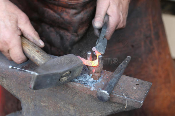 一位年长的铁匠用锤子和锤子打铁的手