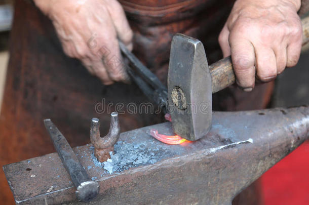 一位年长的铁匠用锤子和锤子<strong>打铁</strong>的手