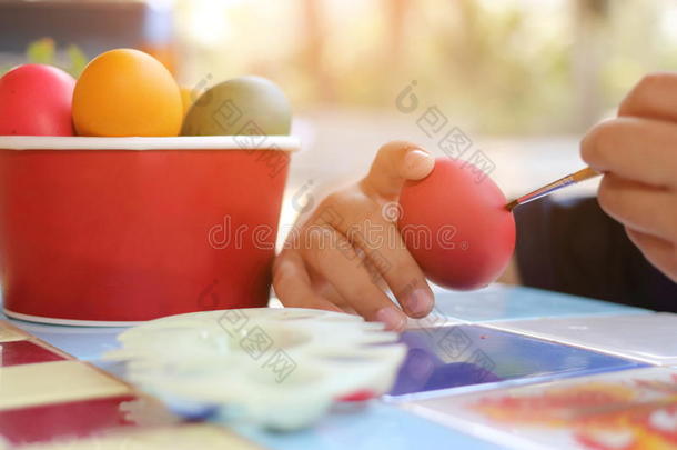 把孩子们的手用画笔涂彩蛋，在大自然模糊的背景上准备复活节。 阳光效应。