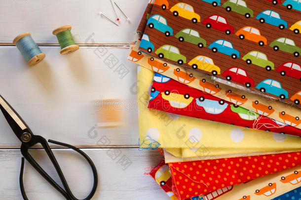 彩色织物与老式剪刀，别针，测量磁带和滚动棉线在白色木桌上