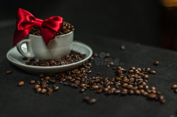芳香咖啡豆在白色杯子里装饰着红色的蝴蝶结，<strong>洒下</strong>咖啡豆