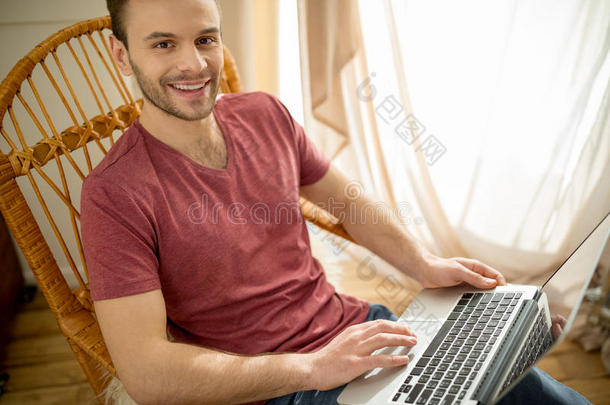 英俊的男人，拿着笔记本电脑坐在摇椅上，对着相机微笑