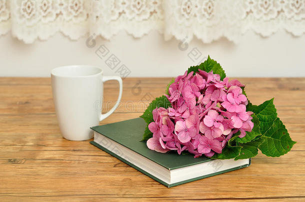 一朵粉红色的绣球花，一本绿色的故事书和一个杯子