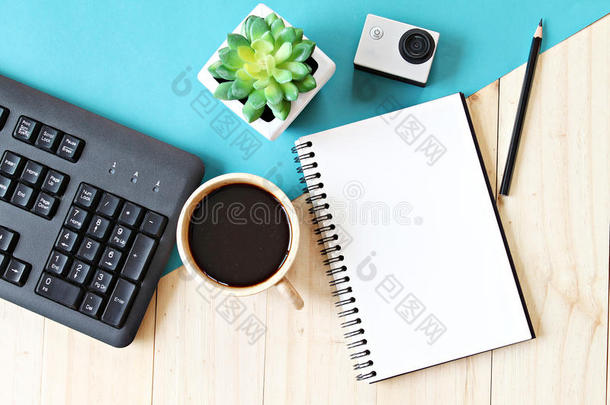 平面布局风格的办公工作空间办公桌与空白笔记本纸，电脑键盘，咖啡杯和行动相机