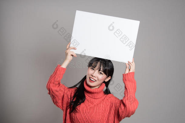 一幅20多岁的亚洲妇女的<strong>摄影</strong>棚肖像，她拿着一块<strong>广告</strong>牌，微笑着