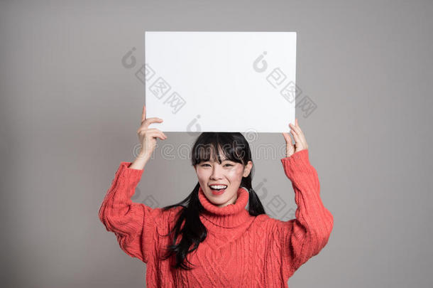 一幅20多岁的亚洲妇女的摄影棚肖像，她拿着一块广告牌，微笑着