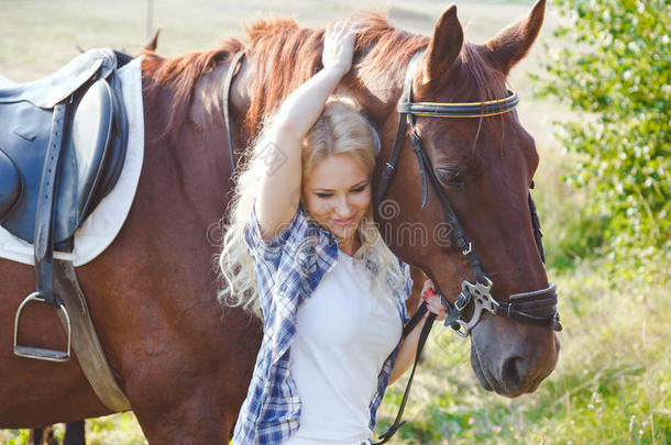 美丽的金发女孩拥抱她的棕色马。 夏季照片以温暖的色调。