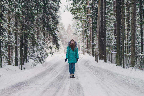 穿着蓝色外套的女孩在寒冷的冬天森林的路上。 女人的冬天心情愉快