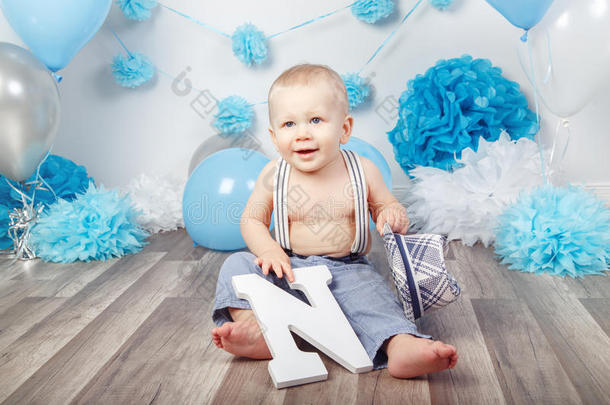 蓝眼睛的小男孩赤脚穿带吊带和帽子的裤子，坐在工作室的木地板上，拿着<strong>大字</strong>母n，Loo