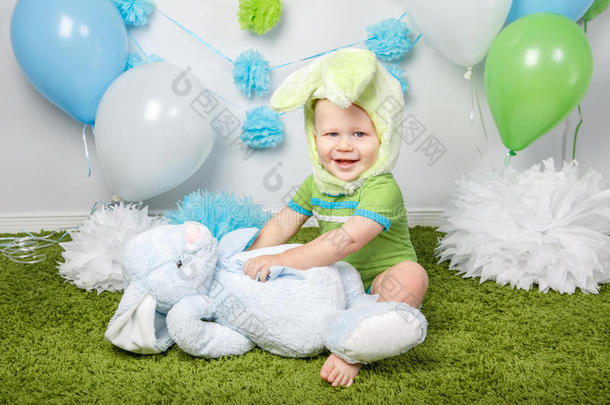 小男孩穿着节日复活节兔子服装，大耳朵，穿着绿色衣服，坐在地毯上