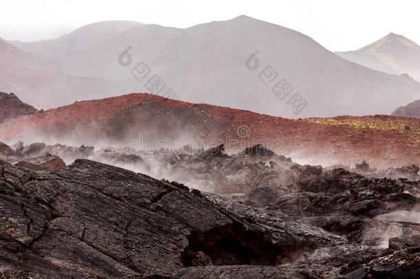贫瘠的熔岩田在小雨中冒着热气，后面有火山