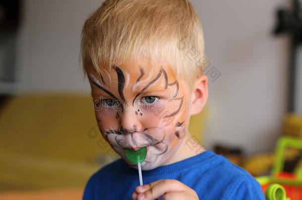 男孩脸上画着橙色的狮子，舔着棒棒糖