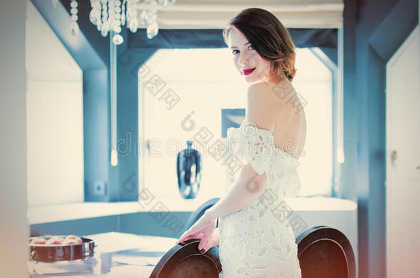 美丽的年轻女人站在轻奢的房间里的桌子旁边，摸着<strong>一把椅子</strong>