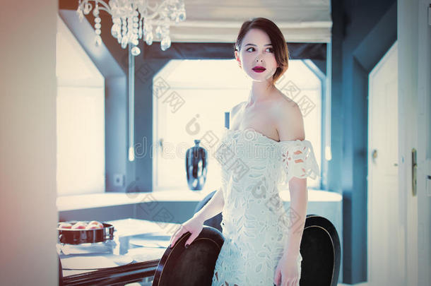 美丽的年轻女人站在轻奢的房间里的桌子旁边，摸着一把椅子