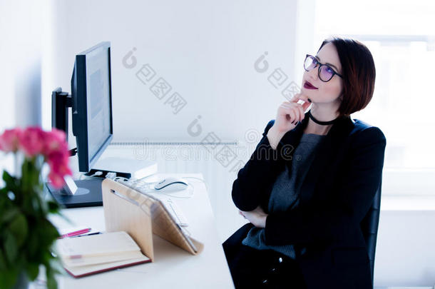 美丽的年轻女人坐在桌子旁，在公司里思考