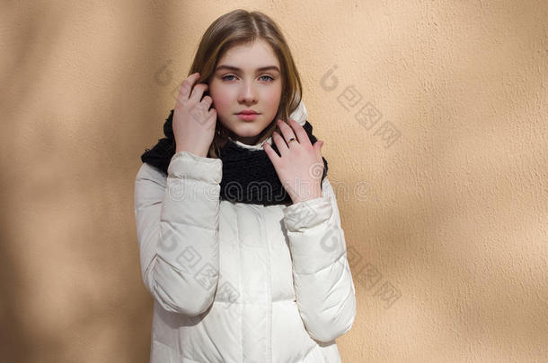 冷季年轻美丽的女人穿着白色外套，摆在纹理墙壁上，有光影图案的生活方式概念肖像