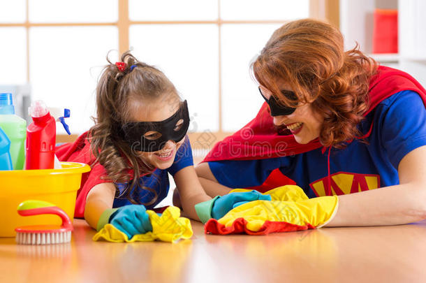 可爱的女人和她的小女儿穿得像超级英雄，打扫地板，微笑