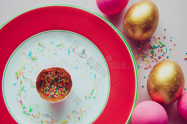 五颜六色的粉红色和金色复活节鸡蛋与糖果洒在盘子上
