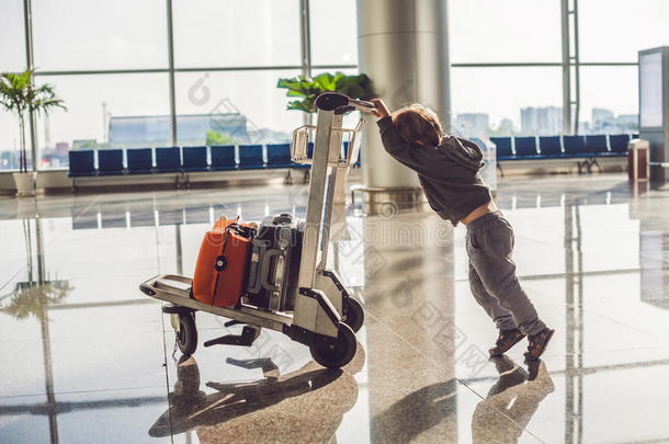 可爱的小男孩，带着橙色的手提箱在机场。 手推车和机场上的男孩