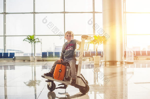 可爱的小男孩，带着橙色的手提箱在机场。 手推车和机场上的男孩