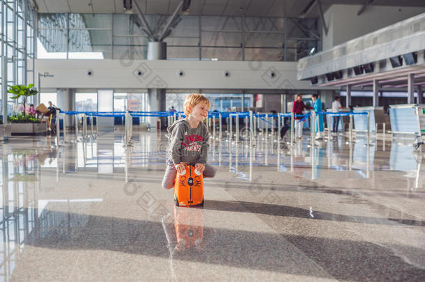 可爱的小男孩在机场提着橙色的手提箱