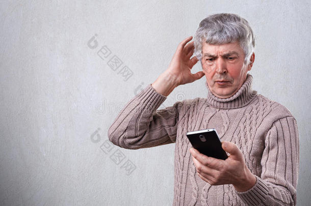 一个惊讶的老人惊讶地用智能手机看新闻。 担心的老人在智能手机上阅读短信