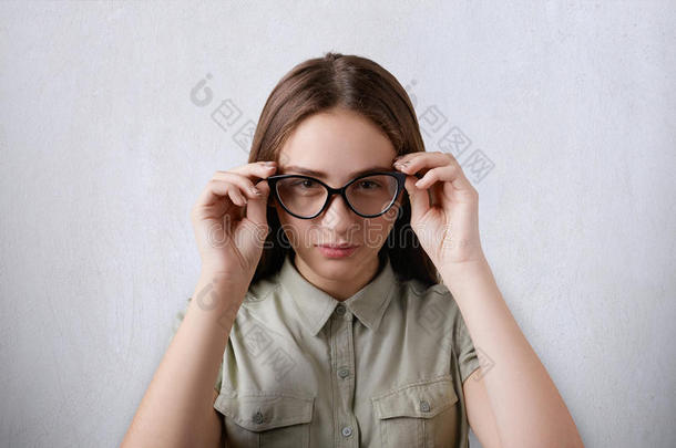 一幅美丽的女孩的肖像，她穿着衬衫，长发被隔离在灰色背景上，戴着一副大眼镜，抚摸着她的眼镜