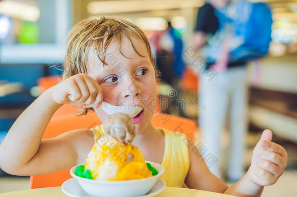 可爱的金发小男孩夏天在城市咖啡馆吃冰激凌