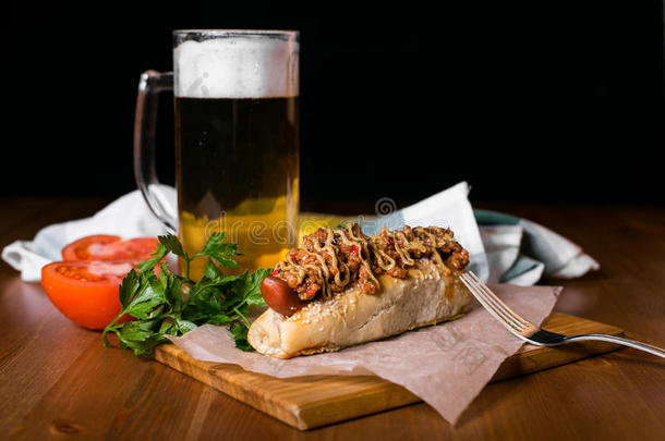 美国热狗与一杯啤酒与甜泡。 热狗和薯片在黑暗的背景下摆在桌子上。