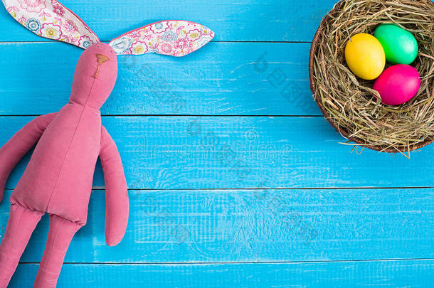 复活节背景与鸡蛋在巢和玩具兔子在蓝色木制背景。 顶部视图与复制空间。
