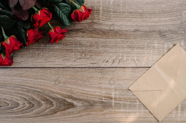 一束红玫瑰放在一张木桌上，上面有一个信封和一张空白的纸卡，作为你的文字
