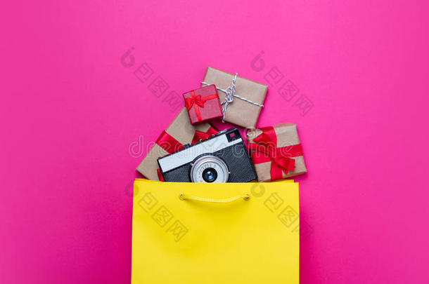可爱的礼物和凉爽的相机在购物袋和酷的笔记本电脑在美妙的粉红色背景