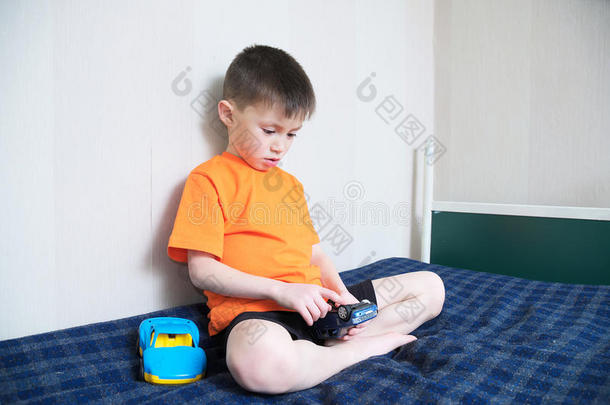 男孩玩汽车游戏，男孩玩玩具坐在床上室内，孩子独自拿着两辆玩具车