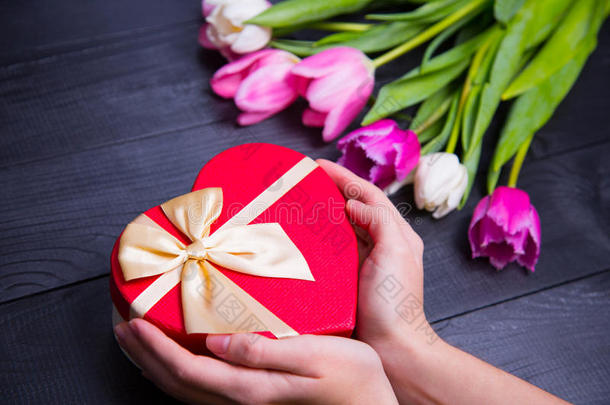 一束嫩粉色的郁金香，拿着黑色木制背景上的礼品盒