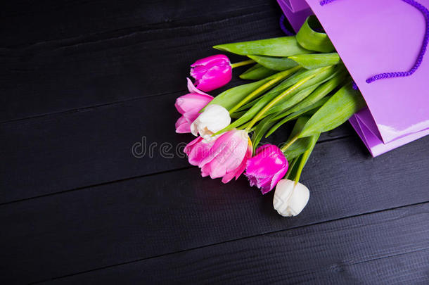 黑色木制背景上<strong>紫色购</strong>物袋中的一束嫩粉色郁金香