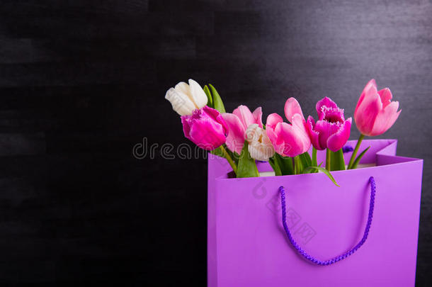 黑色木制背景上紫色购物袋中的一束嫩粉色郁金香