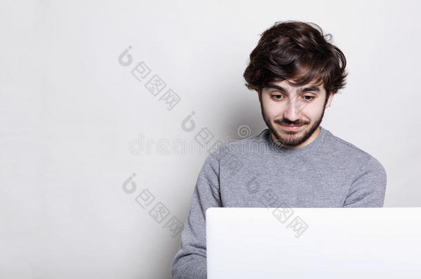 一个惊讶的留着胡须的时髦人，现代发型坐在家里的笔记本电脑前，使用wi-fi，看上去很惊讶。 哼