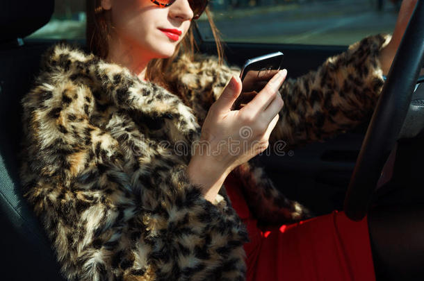 漂亮的女人穿着毛皮大衣，嘴唇红，使用智能手机