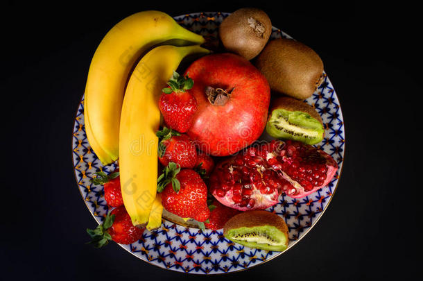 展示新鲜的天然水果，有机草莓，一半石榴石，香蕉和猕猴桃在老式俄罗斯瓷盘，黑色