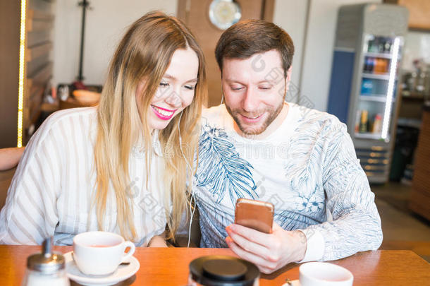 在咖啡吧用手机听音乐的情侣特写。 男人和女人用耳机听音乐。