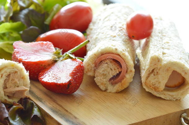 面包卷猪肉腊肠与草莓和蔬菜在砧板上