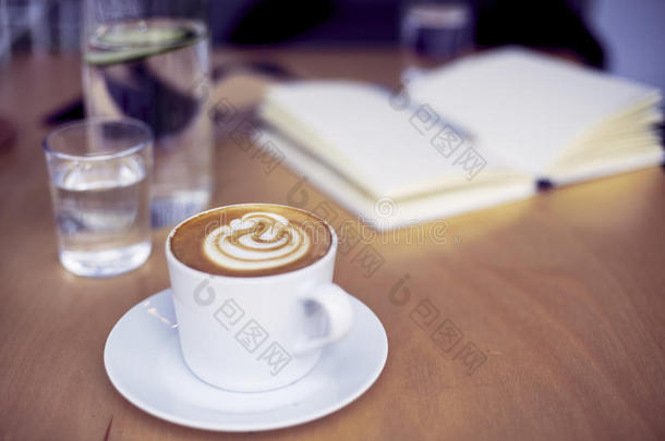 一杯咖啡卡布奇诺，一杯纯净水，木桌上的瓶子，明亮的室内日光
